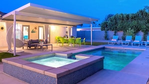 Un'area piscina moderna all'aperto con idromassaggio, posti a sedere e una veranda coperta.