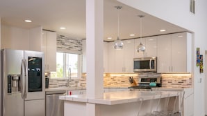 Una cucina moderna con elettrodomestici in acciaio inossidabile, un'isola centrale con sgabelli da bar e illuminazione a sospensione.
