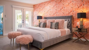 Una camera da letto con un letto, due pouf rosa soffici, una ventola a soffitto e un comodino con una lampada.