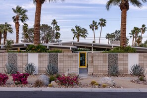 A modern building with a yellow door, surrounded by palm trees and desert plants. - West Elm House 2017: The Alexander (Palm Springs)