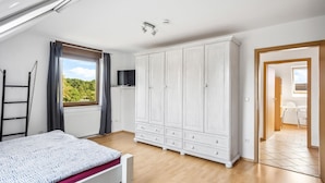 A bedroom with a bed, a wardrobe, a TV, and a window with a view of greenery.