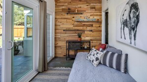 A room with a wooden wall, a glass door, a bed with patterned pillows, a small table with a plant, and a wall-mounted artwork of a cow. - Boho Rhapsody (Palm Springs)