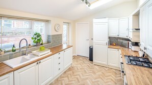 A modern kitchen with white cabinets, a herringbone wood floor, a built-in oven, and a window with blinds. - The Railway Inn MK | Sauna & Jacuzzi | Family & Pet-Friendly | Sleeps upto 8 (Milton Keynes)