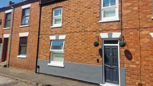 A row of terraced houses with brick facades, white window frames, and a grey door. - The Railway Inn MK | Sauna & Jacuzzi | Family & Pet-Friendly | Sleeps upto 8 (Milton Keynes)