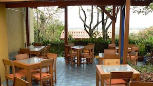An outdoor patio with wooden tables and chairs, surrounded by greenery and a view of the sea. - Villa La Trinidad (San José)