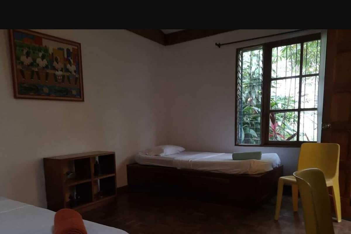 A room with a bed, a chair, a shelf, and a window with a view of greenery.