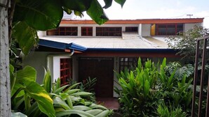 A two-story building with a red roof and white walls, surrounded by lush tropical plants. - Villa La Trinidad (San José)