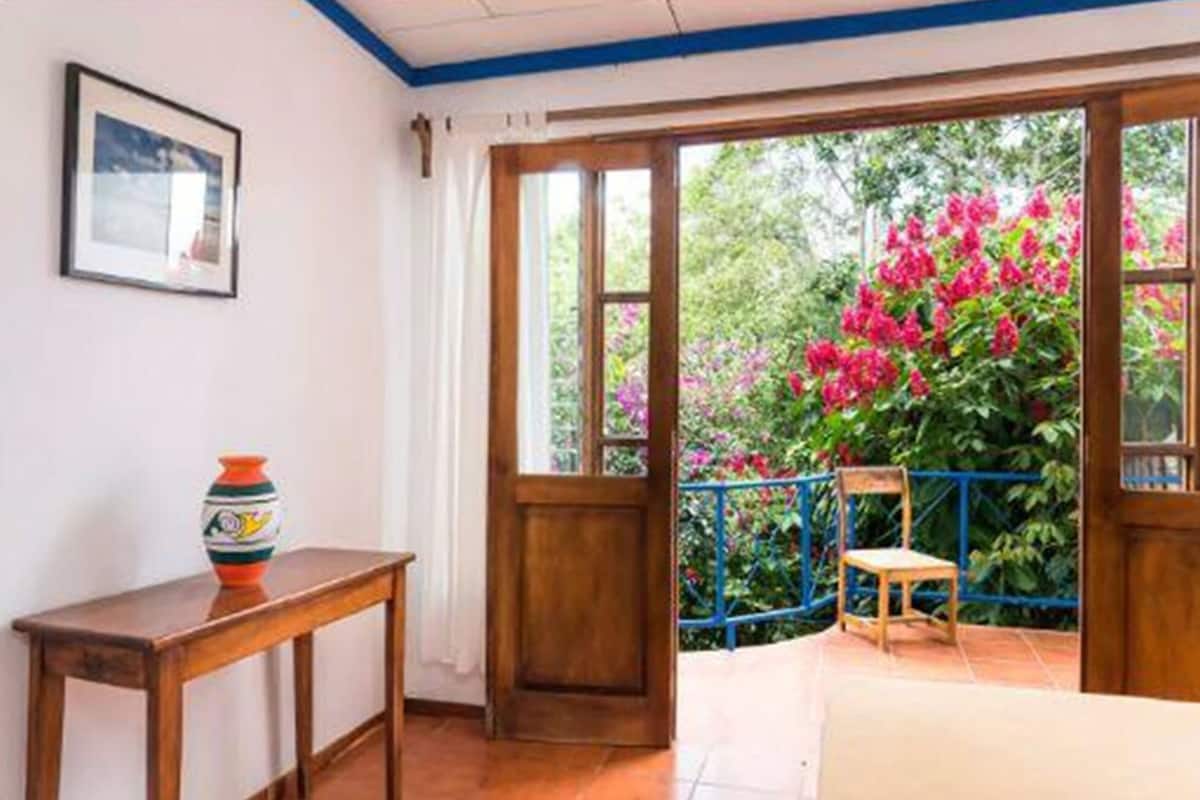 A room with a wooden door leading to a balcony with a view of pink flowers and a blue railing.