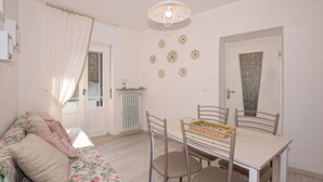 Ein Zimmer mit einem blumigen Sofa, einem Esstisch mit vier Stühlen, einem Heizkörper und dekorativen Tellern an der Wand.