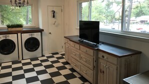 A laundry room with a black and white checkered floor, a chandelier, a washing machine, a dryer, and a television on a wooden cabinet.