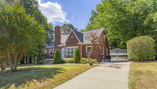 A two-story brick house with a front driveway, a garage, and a well-maintained lawn with trees and shrubs.