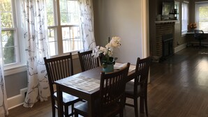 A dining area with a table set for four, surrounded by wooden chairs. There is a vase with flowers on the table, and a chandelier hangs above.
