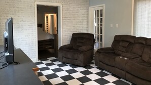 A living room with a black and white checkered floor, two brown sofas, a television, and a brick wall.