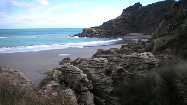 Paesaggio costiero con scogliere rocciose, una spiaggia sabbiosa e l'oceano.