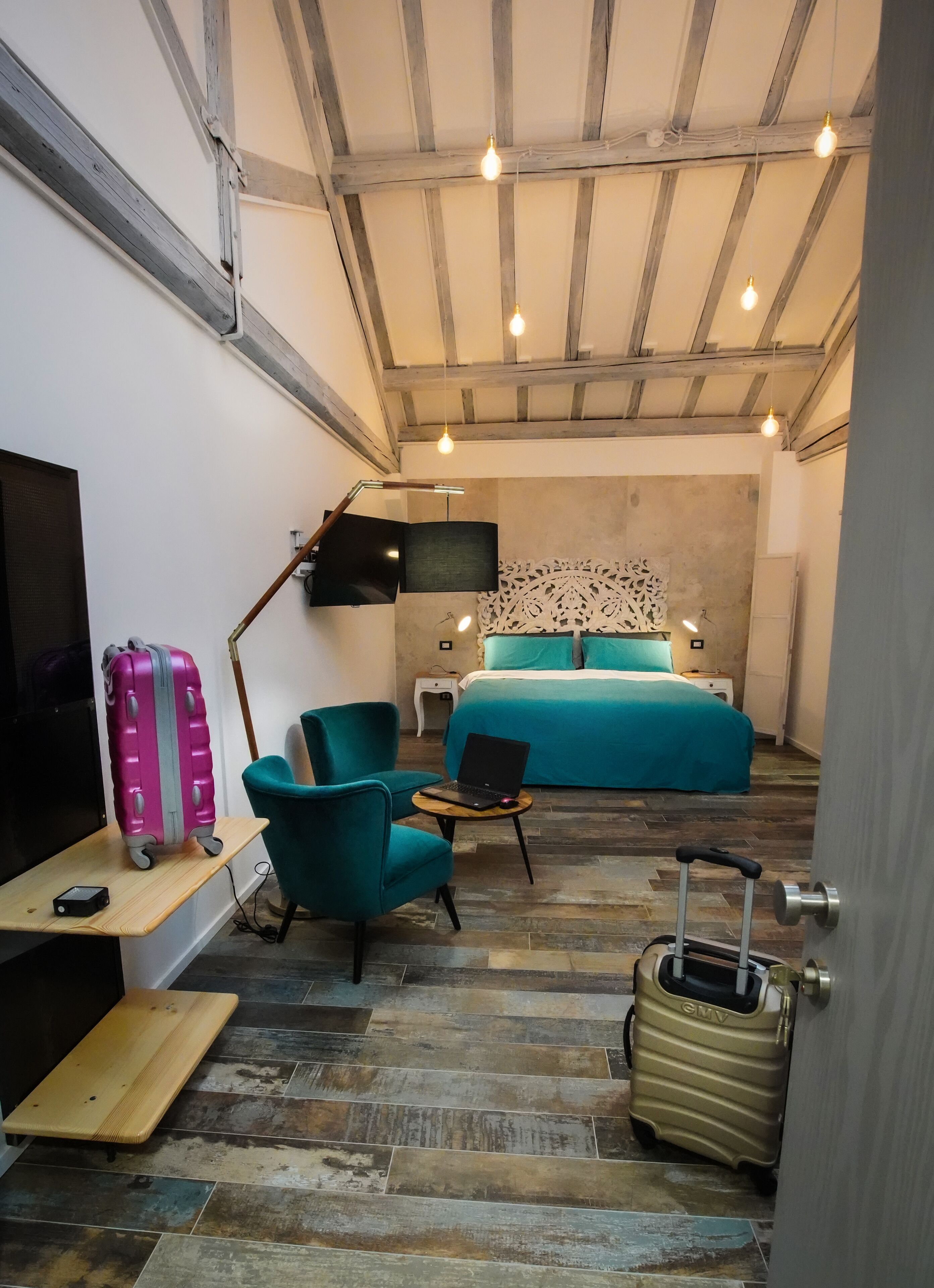 Une chambre d’hôtel de taille réduite, comprenant un lit, un bureau, une chaise, une télévision et une valise.