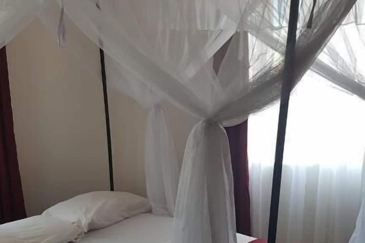 Uma cama de solteiro com dossel branco e roupa de cama vermelha em um quarto com piso de azulejos.