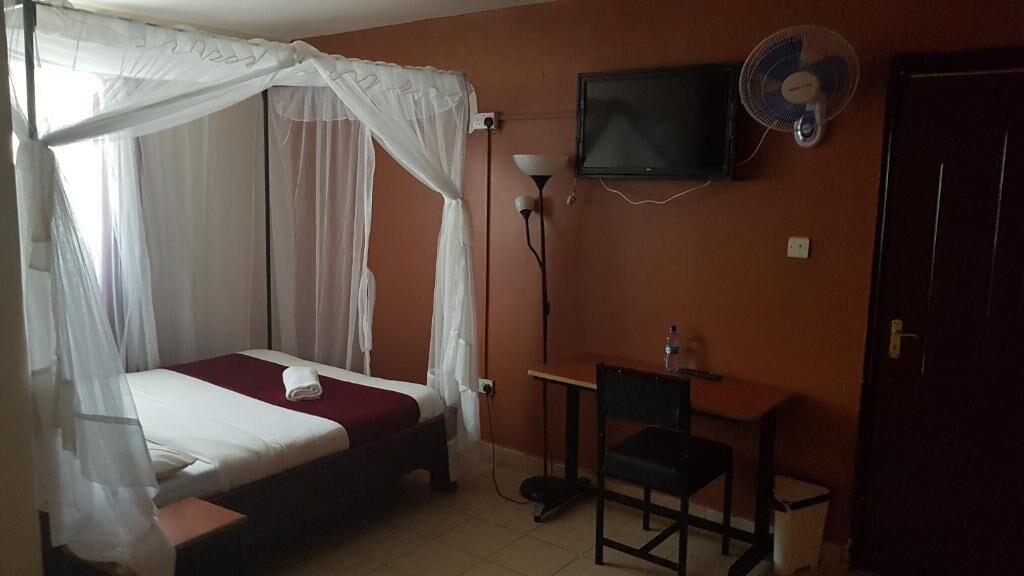 Un dormitorio con cama, escritorio, silla, televisor y ventilador.