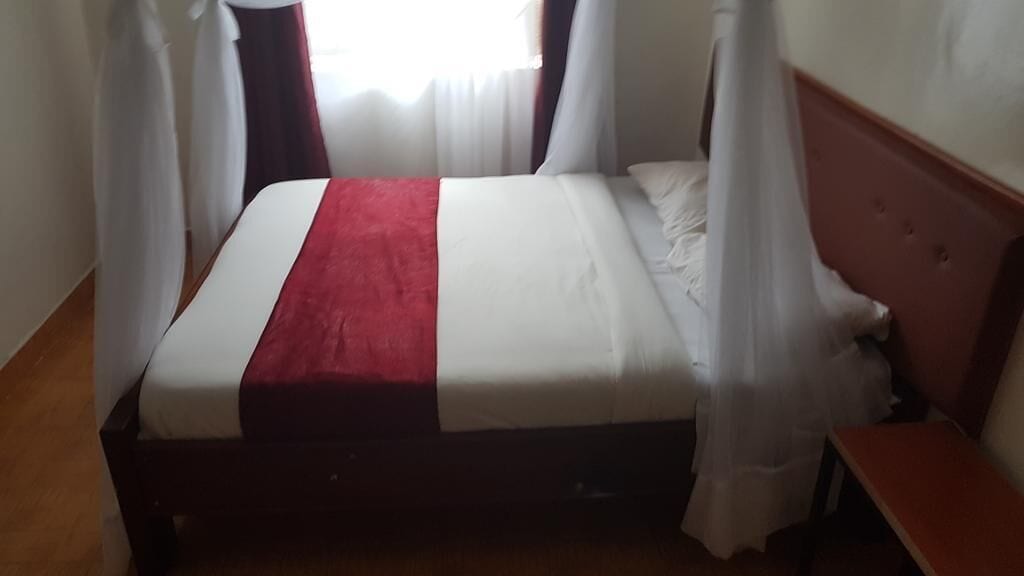 Una cama con colcha blanca y roja, cabecera de madera y cortinas traslúcidas.