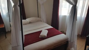 A bed with white bedding and a red blanket, a white towel, and a canopy. - Lila Hotel (Kisumu)