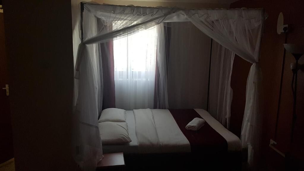 A single bed with a canopy, a bedside table, and a window with sheer curtains.