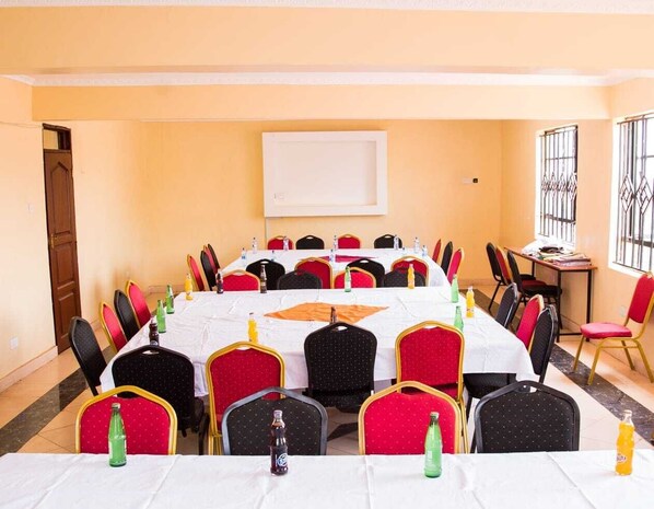 A conference room with a long table, red and black chairs, and a whiteboard on the wall.