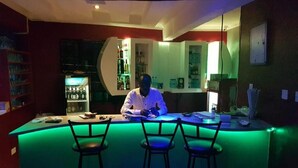 A bar area with a bartender, a neon green bar counter, and two bar stools. - Lila Hotel (Kisumu)