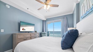 Een slaapkamer met een groot bed, een plafondventilator, een televisie aan de muur en uitzicht op zee door het raam.