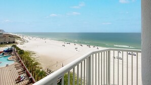Uitzicht op het strand vanaf een balkon met een zwembad en ligbedden.