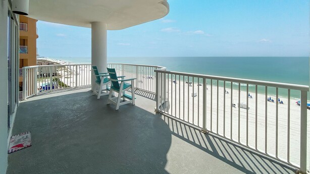 Een balkon met uitzicht op het strand, witte hekken en een tafel met stoelen.