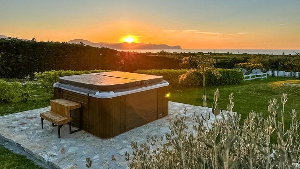 A hot tub with a wooden bench in a garden setting during sunset. - Luxurious home in Partinico (PA) (Partinico (PA))
