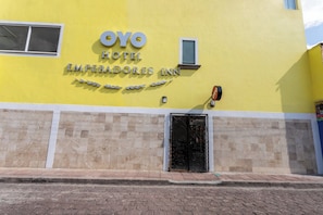 The exterior of OYO Hotel, featuring a yellow facade, a prominent entrance with a black door, and a sign above the door. - Capital O Hotel Emperadores Inn, Atlixco (Atlixco)