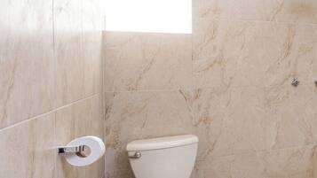 A bathroom with a toilet, a shower, and a marble-tiled wall.