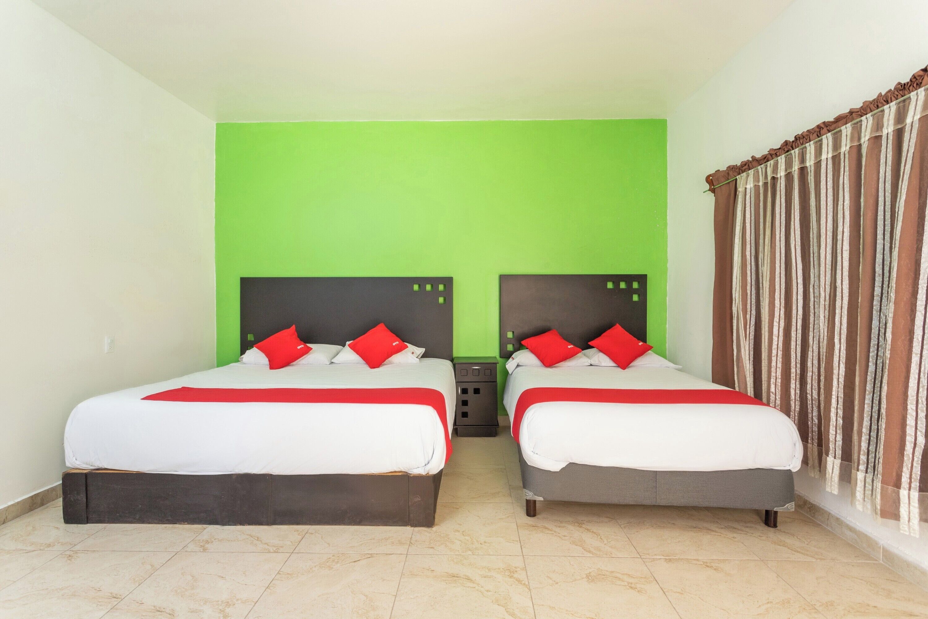 A hotel room with two beds, green walls, and a curtain on the window.