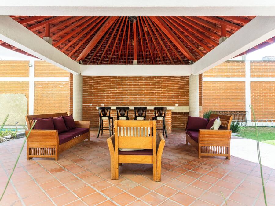 An outdoor patio with wooden furniture, a brick wall, and a red ceiling.