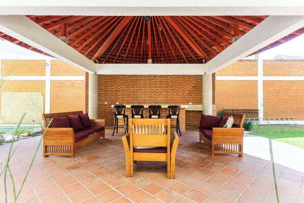 An outdoor patio with wooden furniture, a brick wall, and a red ceiling. - Capital O Hotel Emperadores Inn, Atlixco (Atlixco)