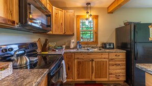Una cocina con armarios de madera, una estufa de acero inoxidable, un refrigerador y una ventana con vistas a zonas verdes.