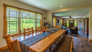 Un comedor amplio con una larga mesa de madera, numerosas sillas y grandes ventanales que ofrecen vistas al exterior.