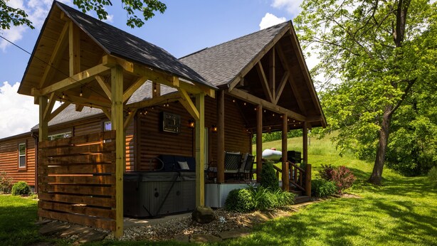 Una cabaña de madera con porche cubierto, mobiliario exterior y un jacuzzi.