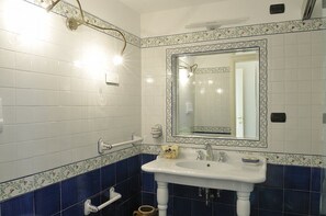 A bathroom with white and blue tiles, a white sink with a mirror above it, and a showerhead.