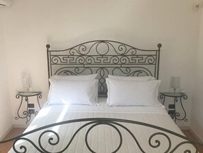 A bed with a decorative metal headboard, two bedside tables with lamps, and a plain wall.