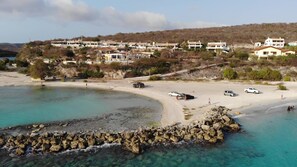 Eine Küstenlandschaft mit Sandstrand, felsiger Küstenlinie und einer Reihe von Gebäuden im Hintergrund.