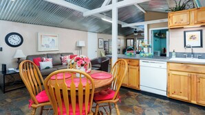 A spacious living area with a dining table, chairs, and a kitchen area with wooden cabinets and a dishwasher. - Creekside Retreat - Charming Cabin w/Deck, A/C, Firepit, & Billy Creek View (Pinetop-Lakeside)