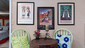 A room with two green chairs, a round table with a vase of flowers, and three framed artworks on the wall. - Creekside Retreat - Charming Cabin w/Deck, A/C, Firepit, & Billy Creek View (Pinetop-Lakeside)