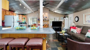 A compact kitchen with a refrigerator, wooden cabinets, and a countertop with fruit baskets. - Creekside Retreat - Charming Cabin w/Deck, A/C, Firepit, & Billy Creek View (Pinetop-Lakeside)
