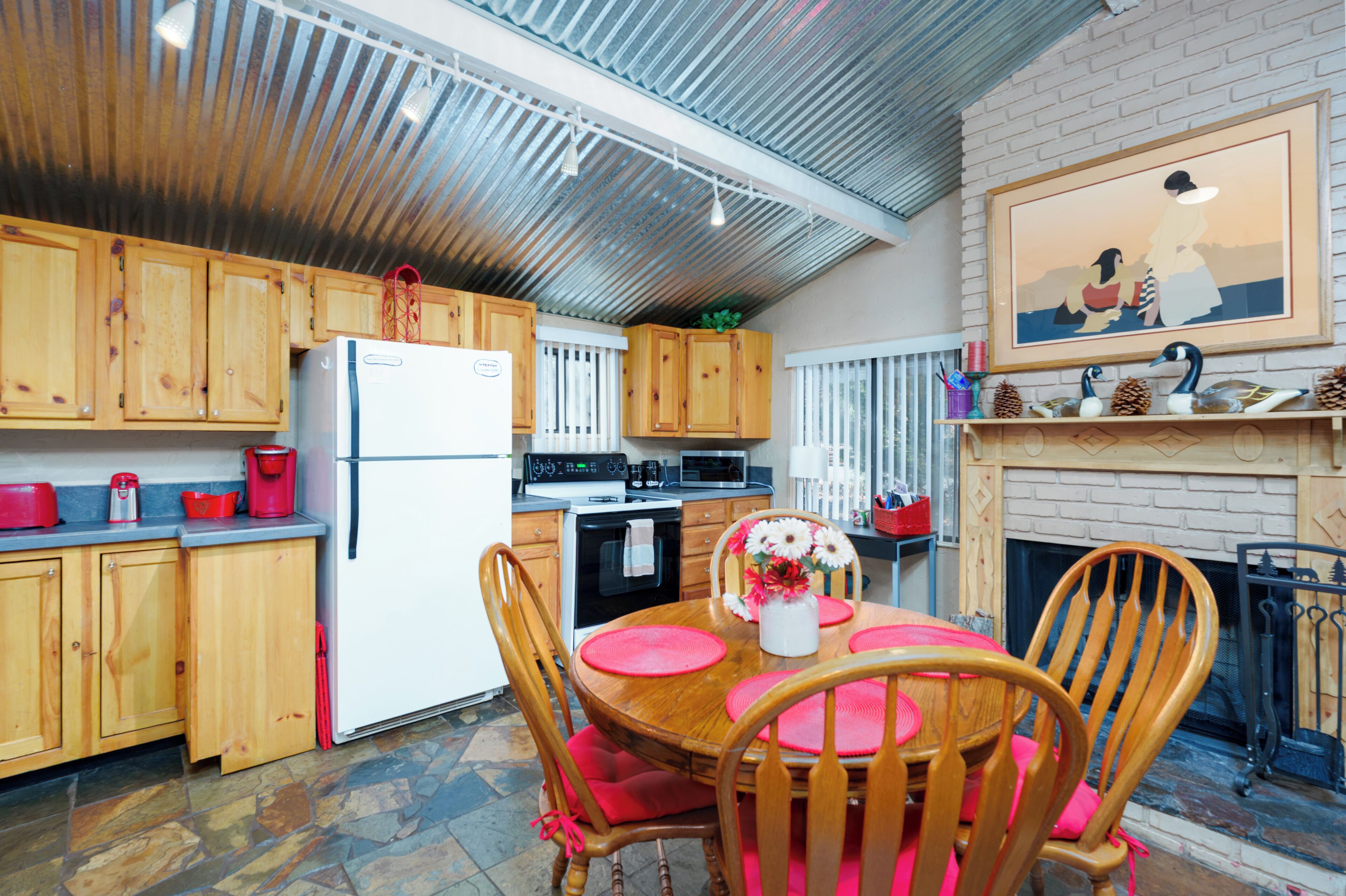 Een keuken met houten kastjes, een koelkast, een eettafel met stoelen en een open haard.