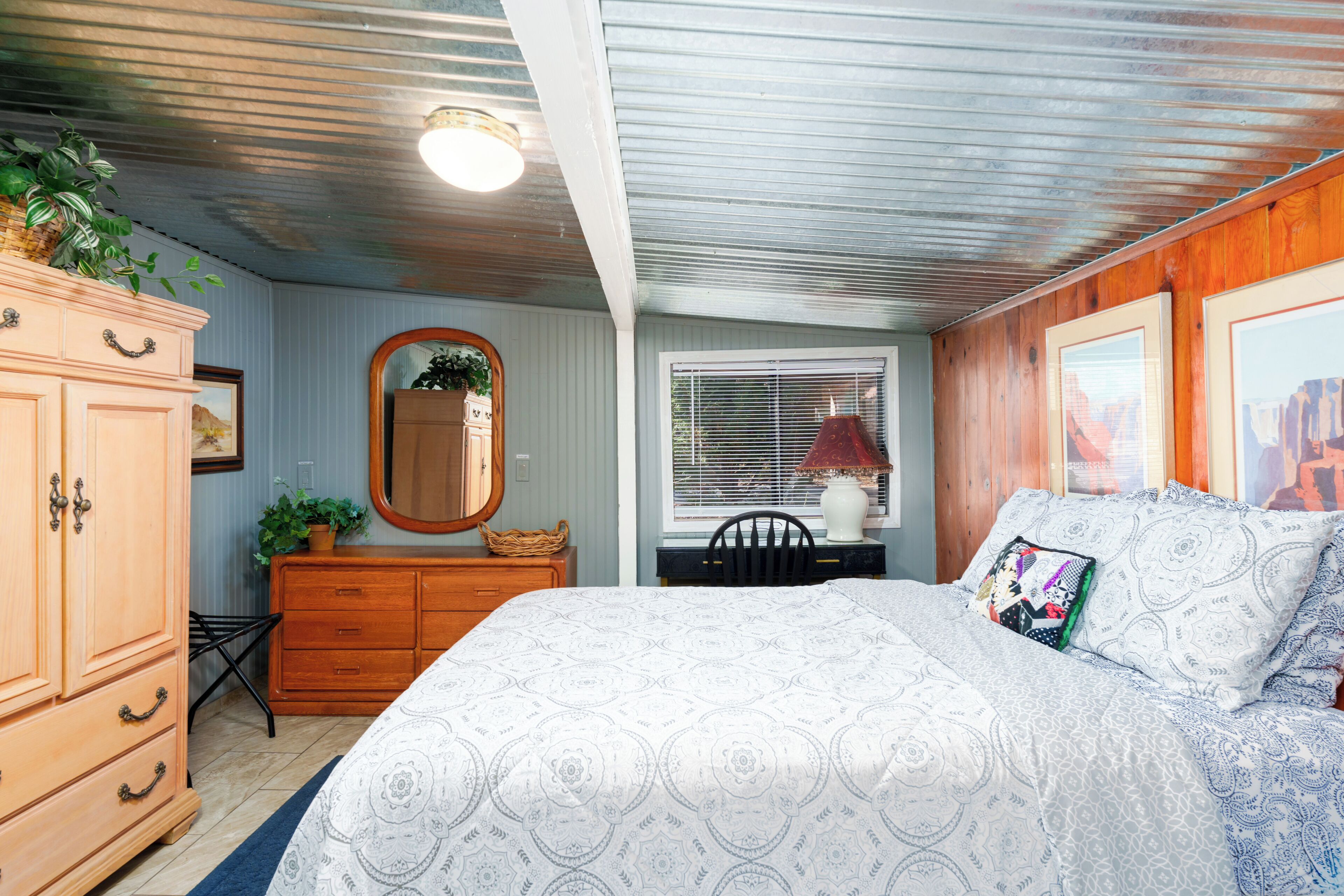 A bedroom with a large bed, a dresser, a mirror, and a window with blinds.