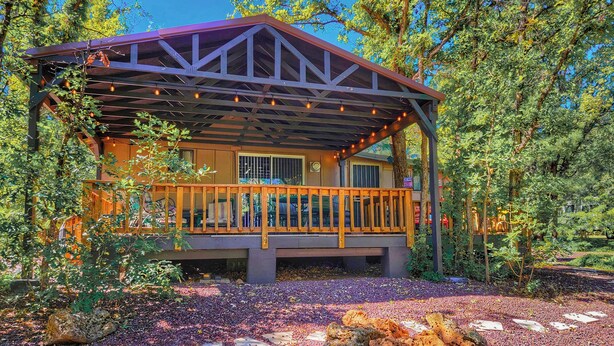 A wooden cabin with a covered porch, surrounded by trees and a gravel path. - Creekside Retreat - Charming Cabin w/Deck, A/C, Firepit, & Billy Creek View (Pinetop-Lakeside)