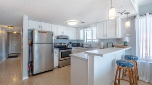 Une cuisine moderne avec des meubles blancs, des appareils en acier inoxydable et un îlot central doté de tabourets de bar.