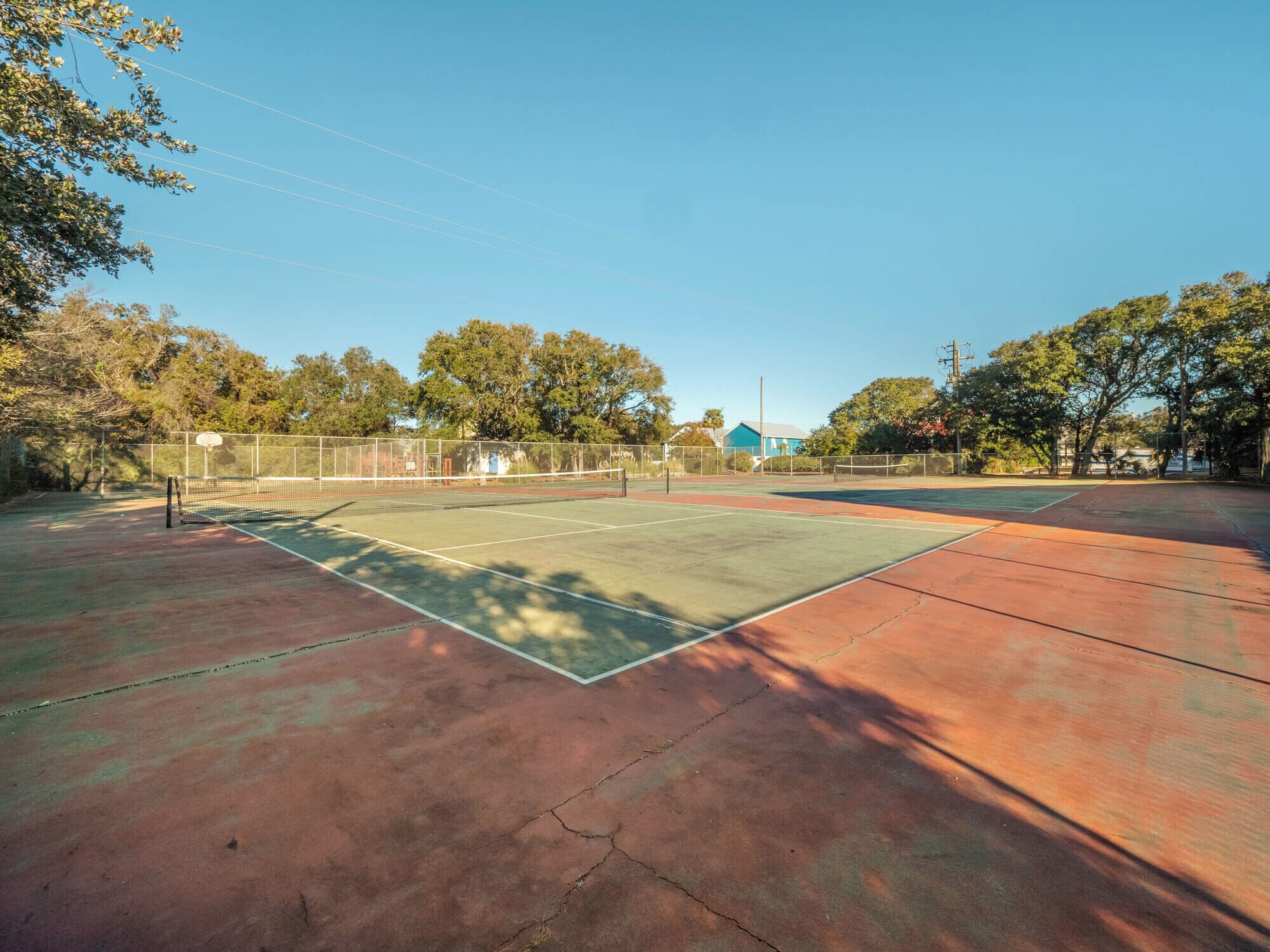 An outdoor tennis court with a net, surrounded by trees and a fence.