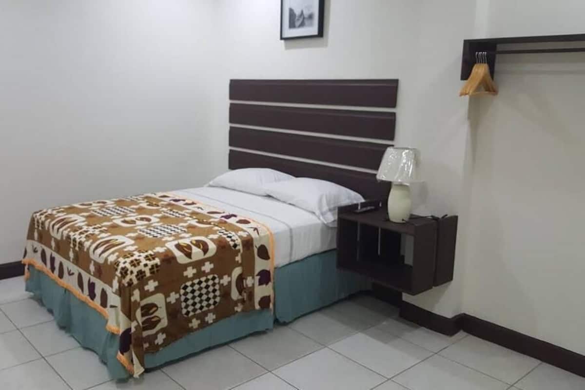 Un dormitorio ordenado con cama, mesita de noche y estante en la pared.